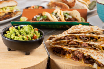 A view of a table filled with a variety of popular Mexican entrees, featuring a quesadilla, in a restaurant or kitchen setting.