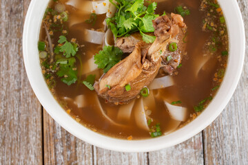 A top down view of a bowl of duck  soup with flat noodles.