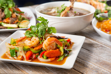 A view of several Thai dishes on a wooden table surface, featuring a shrimp cashew salad entree.