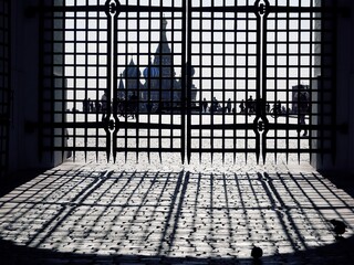 Black openwork gates casting a shadow on the ground, behind which the Moscow Kremlin can be seen