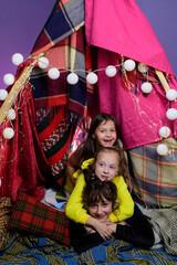 Kids embrace in home-made tent inside the living room before going to sleep. Child pajama party. Pajamas for kids. Little Girls in tipi house. Sisters or best friends spend time. © Volodymyr