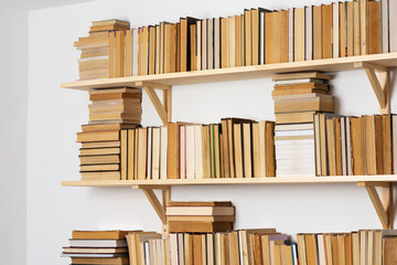 Light wooden bookshelves with hardback overturned books in white interior, home library