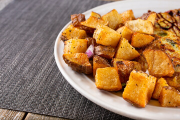 A view of a side of roasted potatoes on a plate, cut off on the right side of the frame.