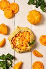 Pie with yellow tomatoes , bell peppers and sesame seeds, galette with vegetables and cheese on white wooden background, top view
