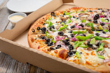 A view of a supreme pizza inside a delivery box, in a restaurant or kitchen setting.