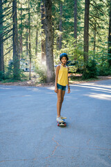 Fototapeta premium Portrait of smiling teen girl skateboarding on road in forest