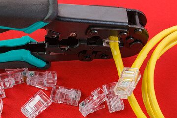 Computer network laying concept. Crimper tool and transparent connectors connectors on red background. Crimper and ethernet cable. Close-up.