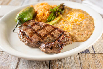 A view of a plate of steak, rice and beans, in a restaurant or kitchen setting.