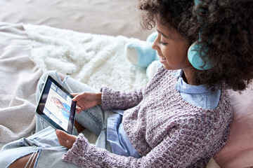 African american kid girl talking to grandmother or distance teacher during online virtual family chat videocall meeting on holiday by video conference call using tablet computer sitting on bed.