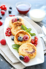 Tasty cheese pancakes with berries, bowls with jam and cream on grey background