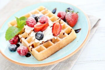 Tasty waffles with fresh berries and whipped cream on white wooden background