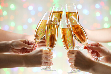 Female hands clink glasses of champagne on blurred lights background