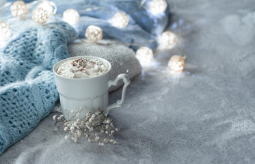 Obraz na płótnie Canvas cozy winter composition with cup of hot chocolate, hot cooca cup with knitted sweater and ball lights, girly winter aesthetic photography, blue and white hues and airy atmosphere