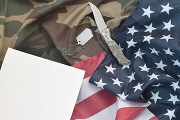 Blank paper lies with knife and army dog tag necklace on camouflage uniform and american flag