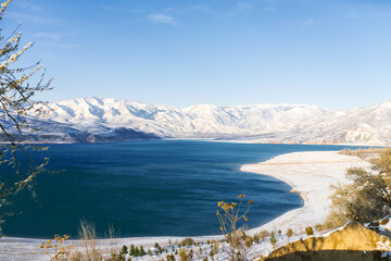 Amazing beautiful winter landscape of Charvak reservoir in Uzbekistan in winter with blue water in it, surrounded by the Tien Shan mountain system