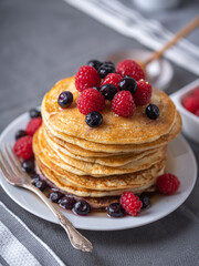 Sweet homemade pancakes with raspberries and blueberries on white plate.