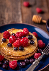Sweet homemade pancakes with raspberries and blueberries on blue plate.