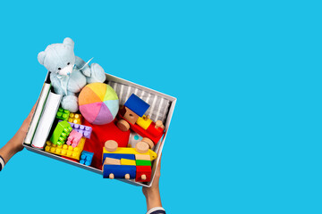 Donation concept. Kid hands with donate box with clothes, books and toys on light blue background....
