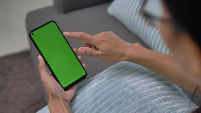 Over shoulder closeup view of asian woman user holding smart phone watching mobile video calling green screen