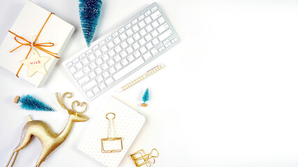 Christmas shopping desktop in modern gold and white theme with reindeer decoration, keyboard, gift and desktop accessories. Top view blog hero header creative composition flat lay.