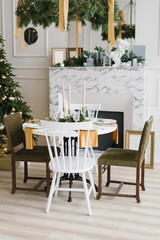 Stylish festive Christmas table with vintage chairs near the marble fireplace and Christmas tree in the living room or dining room in the house