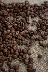Scattered roasted coffee beans on burlap. Close-up. Vertical.