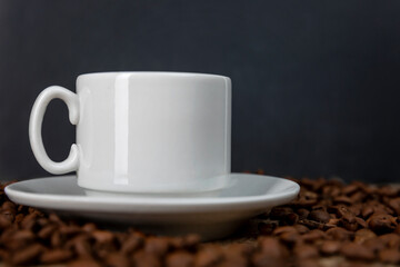 White cup with coffee on sprinkled roasted beans. Black background. Space for text.
