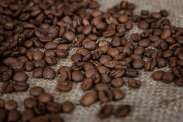 Scattered roasted coffee beans on burlap. Close-up.