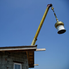 A crane holds the bright golden dome of a Christian church suspended for installation and assembly, or dismantling, on the roof of the temple. Blue sky.
