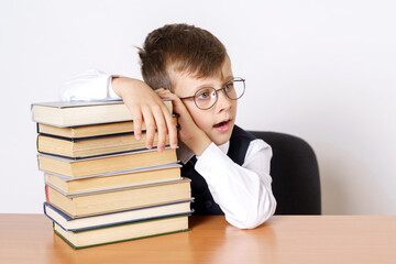 The student sits at the table and holds his head, hands operate on the stacked books, looks to the side. Isolated on white background.