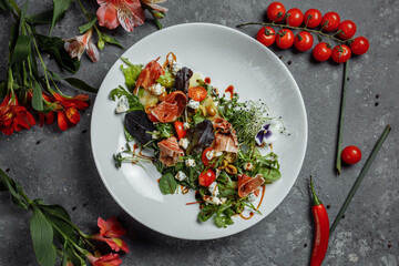 salad with ham and pear on dark gray background. jamon salad, salad mix, spinach, pear, cherry tomatoes, Dor Blue, capers and vinegar dressing Bianco