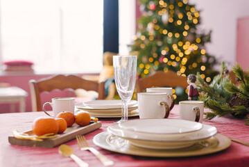 White plates, champagne glasses, tangerines in the serving of a festive dinner for Christmas, Christmas eve against the background of Christmas tree lights