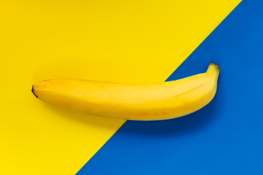 One yellow ripe banana on blue yellow background