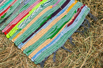 Colorful handmade knitted rug lays on hay