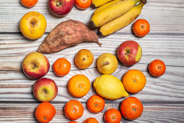 Many orange autumn fruits like mandarins, apples, pears and bananas on a wooden surface