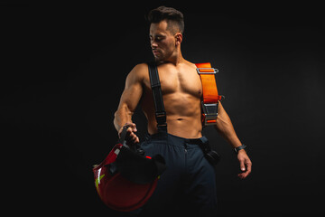 portrait of a muscular, handsome firefighter on a dark background, holding a fire helmet, looking...