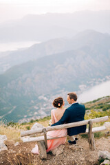 Fototapeta na wymiar bride and groom sitting on the bench on the mountain against the backdrop of the Bay of Kotor