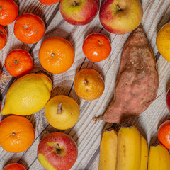 Many orange autumn fruits like mandarins, apples, pears and bananas on a wooden surface