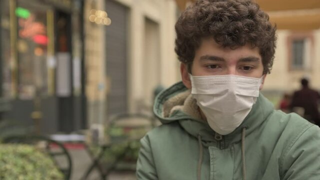 Portrait of a boy at a bar table: Coronavirus requires the use of a mask and sitting away from other people. While waiting to be served, he is absorbed in his thoughts on the pandemic. 