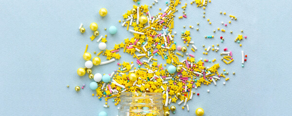 Wide banner Yellow sugar sprinkles grainy on blue background, close-up flat lay