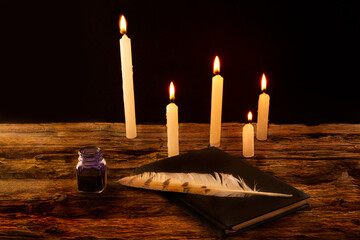 Pluma sobre libro negro con tinta y velas 