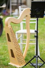 Celtic wooden lap harp on green grass, chair and music stand in backyard without music players
