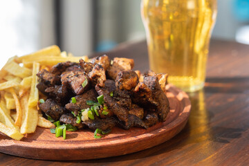 meat entree with french fries on a wooden board and glass of beer