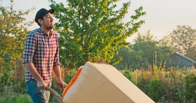 A young farmer carries a sack of dried hops from a warehouse on a trolley at sunrise.