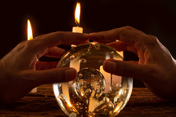 Bola de cristal con manos y velas en fondo negro 