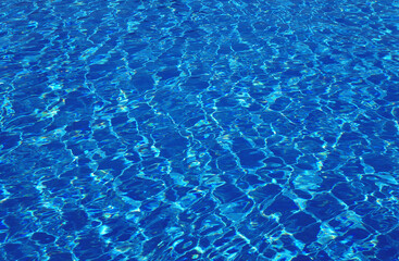 Clear blue pool water with highlights and sun reflections on the surface