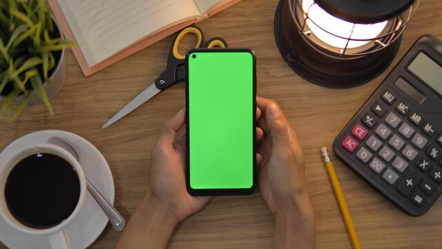 Top view of woman use digital smartphone with green screen. Office desk background. Chroma key. smartphone with green screen in table