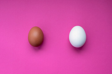 Two chicken eggs - white and brown - on a pink background. Top view.