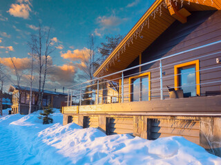 The cottage is covered with snow. The building is decorated for Christmas. Winter evening. House against the backdrop of a beautiful sky. Cottage surrounded by a winter landscape. Sunny day in winter.