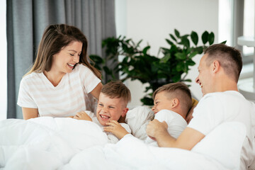 Young family enjoying in bed. Happy parents with sons relaxing in bed..